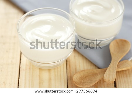 yogurt in glass cup on wooden background with grey cotton and wooden spoon. white yoghurt. 