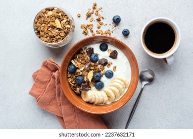 Yogurt with granola, banana, blueberries and dark chocolate chunks in a bowl served with cup of black coffee. Top view healthy breakfast meal - Powered by Shutterstock