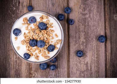 Yogurt with granola and fresh blueberries, in glass bowl over old wood background. Vintage effect.