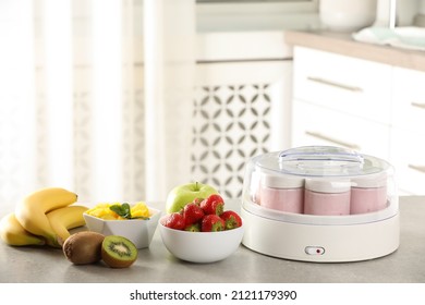 Yogurt maker with jars and different fruits on light grey table in kitchen