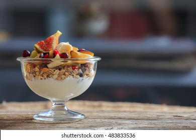 Yogurt, Muesli And Fresh Fruit Salad In A Glass Bowl On A Wooden Table, Front View With Details, Space For Text