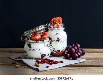 Yogurt and oat granola with grapes, pomegranate and grapefruit in a tall glass jar on black backdrop. Hand pours honey over the jar with a wooden stick - Powered by Shutterstock