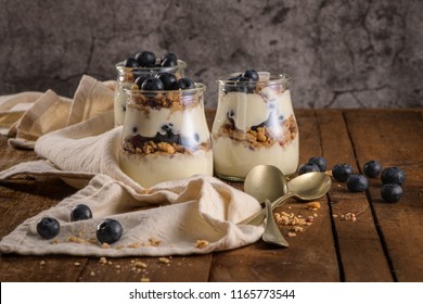 Yogurt Parfait With Blueberry And Granola. Healthy Breakfast Concept Served In Mason Jar With Decorative Spoons On Wooden Table.