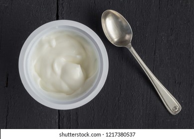 Yogurt In Plastic Cup On Rustic Black Table With Small Silver Spoon - Natural Greek Yoghurt Top View Photo