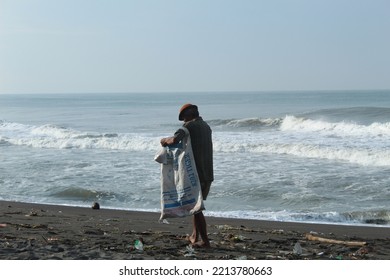 Yogyakarta, Indonesia, February 1, 2022 ; Selective Focus, A Traditional Fisherman Is Cleaning Up Trash On A Black Sandy Beach With Small Waves On A Sunny Day. Photo Is Noise