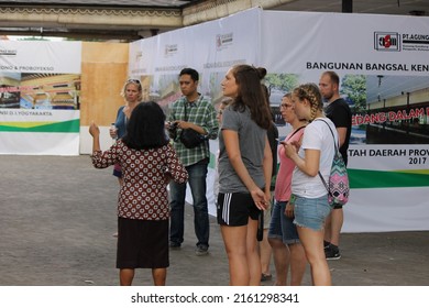 yogyakarta, indonesia-may, 28, 2022: several foreign and local tourists are listening to a tour guide dressed in batik talking and pointing with their hands, photographed in outdoor natural light 