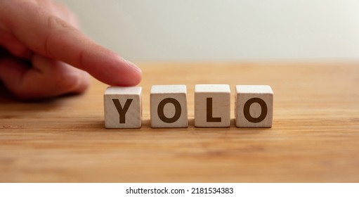 Yolo concept. Word yolo on wooden cube with finger to shows letter y. You Only Live Once phrase, message to seize the day, positive lifestyle, follow your dream, life is your live it.