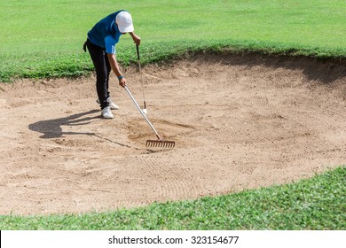 Yong asia golfer raking bunker after shot. - Powered by Shutterstock