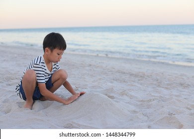 Yong Asian Boy Is  Building Sand Castle Alone On The Beach.