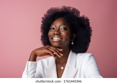 Yong beautiful happy smiling African American woman, model wearing elegant jewelry, white blazer, posing in studio, on pink background. Close up portrait. Copy, empty space for text