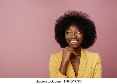 Yong beautiful happy smiling African American woman, model wearing elegant jewelry, yellow blazer, posing in studio, on pink background. Copy, empty space for text  - Powered by Shutterstock