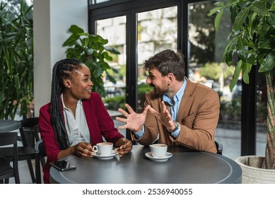 Yong happy business people, office workers, businessman and businesswoman sitting together in cafeteria, drinking coffee, taking a break from work, talking and discussing ideas and life themes. - Powered by Shutterstock