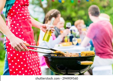 Yong Man At The Bbq Grill Turning The Meat, In The Background Friends Are Having Garden Party