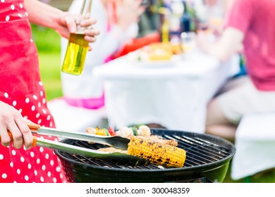 Yong Man At The Bbq Grill Turning The Meat, In The Background Friends Are Having Garden Party