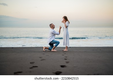 Yong man making a marriage proposal on a beach at sunset to a young beautiful woman. Standing on on knee. - Powered by Shutterstock