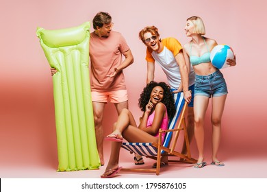 Yong Multiethnic Friends In Swimsuits And Sunglasses With Inflatable Ball And Mattress On Pink Background