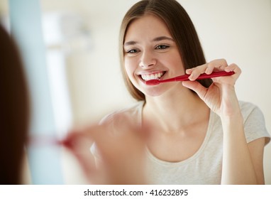 Yooung woman brushing her teeth at mirror