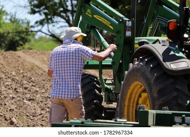 York, Ontario / Canada - June 8, 2020: Local Farmer Examining His John Deere Tractor As He Prepares To Plow Soil. 