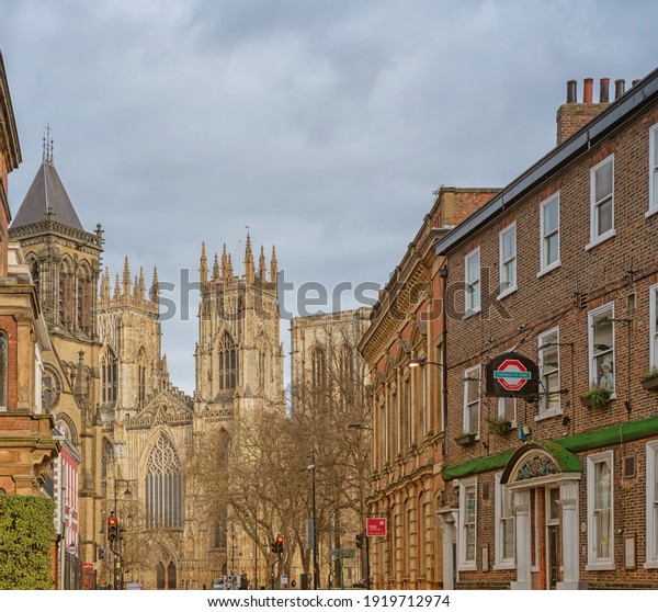 York, UK. February 12, 2021. York\
Minster and St Wilfrid’s Church from Museum Street in York.  There\
are buildings on either side and a cloudy sky\
above.