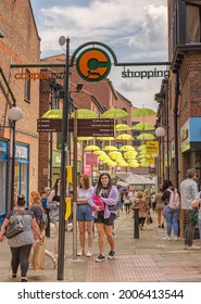 York, UK. July 2, 2021.  A Pedestrianised Street With An Overhead Display Of Yellow Umbrellas.  There Are Shops On Either Side And Shoppers Walk Up And Down.