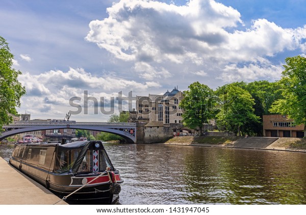 York UK. June 18, 2019. The River Ouse in\
York.  A barge is in the foreground and the historic Lendal Bridge\
and city buildings are in the\
distance.