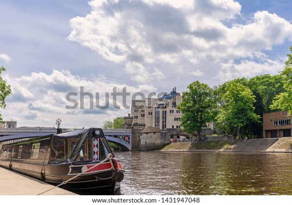 York UK. June 18, 2019.  The River Ouse in\
York.  A barge is in the foreground and the historic Lendal Bridge\
and city buildings are in the\
distance.
