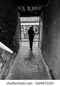 YORK, UK - SEPTEMBER 21, 2019: Man At Silhouetted In The Bright Light At The End Of A Dark Shadowy Alleyway. Black And White. 