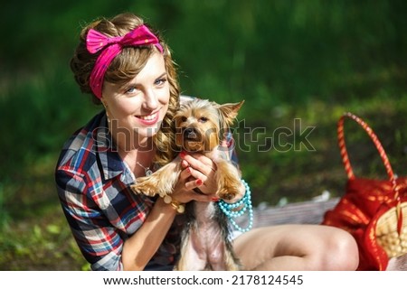 yorkshire terrier small dog in arms of beautiful young girl in a plaid shirt and short denim shorts in pin-up style in forest
