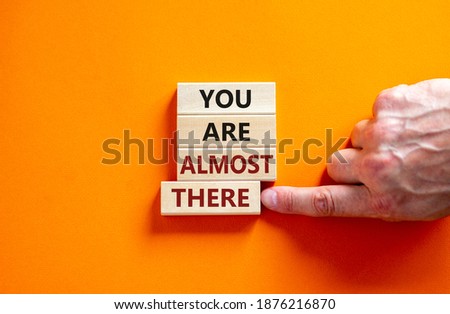 You are almost there symbol. Wooden blocks form the words 'You are almost there' on beautiful orange background. Male hand. Business and you are almost there concept, copy space.