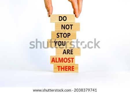 You are almost there symbol. Wooden blocks with words 'do not stop you are almost there'. Businessman hand. Beautiful white background, copy space. Business, motivation and almost there concept.