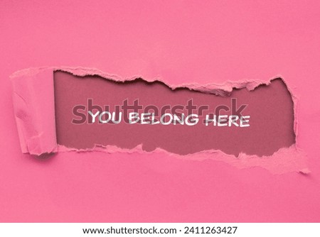 You belong here lettering on ripped pink paper with pink background. Conceptual business photo. Top view, copy space for text.