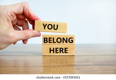 You belong here symbol. Wooden blocks with words 'You belong here' on beautiful wooden table, blue background. Businessman hand. Diversity, business, inclusion and belonging concept. - Shutterstock ID 1927093451