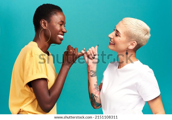 You can count on\
me. Studio shot of two young women linking their fingers against a\
turquoise background.