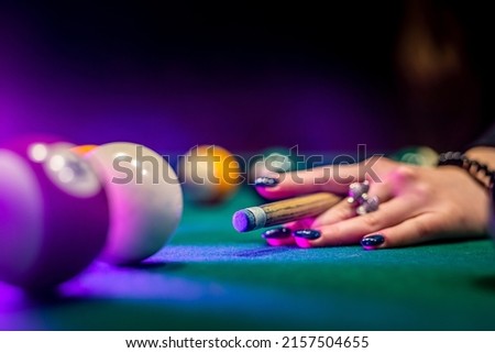 you can see beautiful female hands in black clothes deftly holding a cue and trying to drive a billiard layer into the hole. Billiards sport game concept