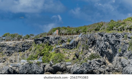 You can see a colorful wooden ladder on a steep cliff, dark blue sea water with a clear sky. - Powered by Shutterstock