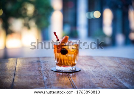 you can see a rum old fashioned on ice cocktail on a wooden table the color of which is orange transparent with a blurred background