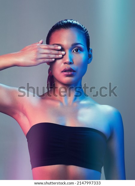 You cant but help to take a look at
her. Studio portrait of a beautiful young woman posing while
holding her one eye closed against a multi colored
background.