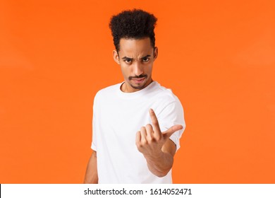 You Come Here Now. Serious Bossy And Strict, Confident Man With Angry Expression, Frowning Looking Under Forehead And Flick Index Finger As If Inviting, Demand Person Step Foward, Orange Background