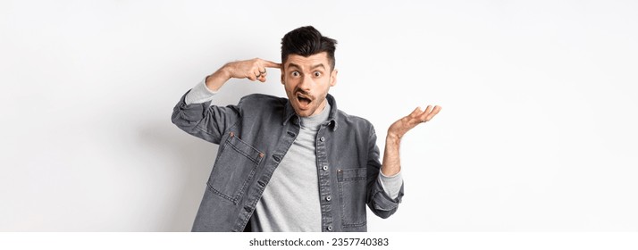 Are you crazy. Angry man scolding person for stupid actions, pointing at head temple and raising hand confused, complaining while standing on white background.