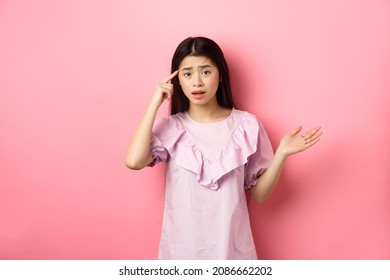 Are You Crazy. Shocked Asian Woman Pointing At Head Temple And Complaining Someone Stupid Action, Scolding Person, Standing Against Pink Background