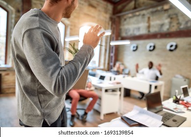 If you don't like something change it. Young man in casual wear holding box with personal things and saying good bye to his ex-colleagues while leaving modern office. Quit concept. Office life