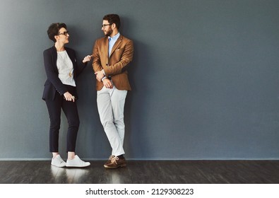 You gain so much from mingling. Shot of two designers having a conversation while leaning against a wall. - Shutterstock ID 2129308223