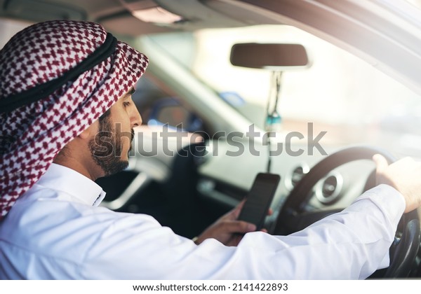 You have reached\
your destination. Shot of a young muslim businessman using his\
phone while driving a car.