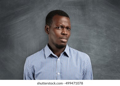 Are You Serious? Irritated Young Dark-skinned Teacher Or Student Dressed In Checkered Shirt, Looking Dissatisfied And Surprised, Standing Against Blackboard With Copy Space For Your Advertisement