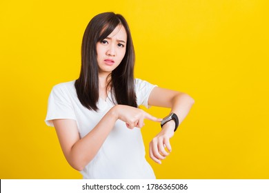 You are late not on time, Portrait Asian of a happy beautiful young woman scared casual girl showing and pointing finger her wristwatch studio shot isolated on yellow background