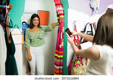 You Look Stunning! Young Woman Taking Pictures With A Smartphone Of Her Best Friend Trying On New Outfits At The Clothing Store