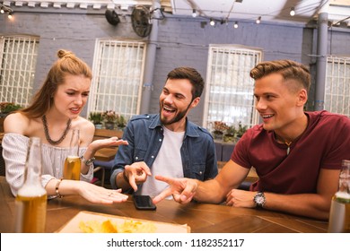 You lose. Cheerful young men looking at their friend while playing table games together
