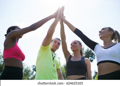 You are my champions. Group circle of  happy athletic young women in sportswear holding hands together with coach in green summer park  outdoors - Powered by Shutterstock