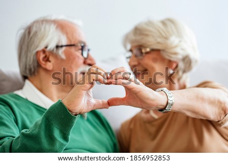 You are my heart. Portrait of cute and cheerful senior couple making a heart shape with their hands and fingers while standing together at home.  Senior couple showing hand heart gesture