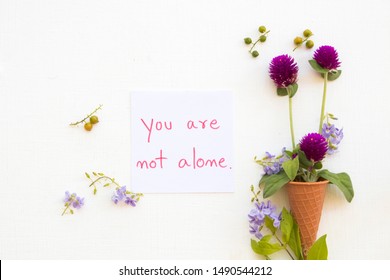 you are not alone message card handwriting with purple flower amaranth in cone arrangement flat lay postcard style on background white wooden
